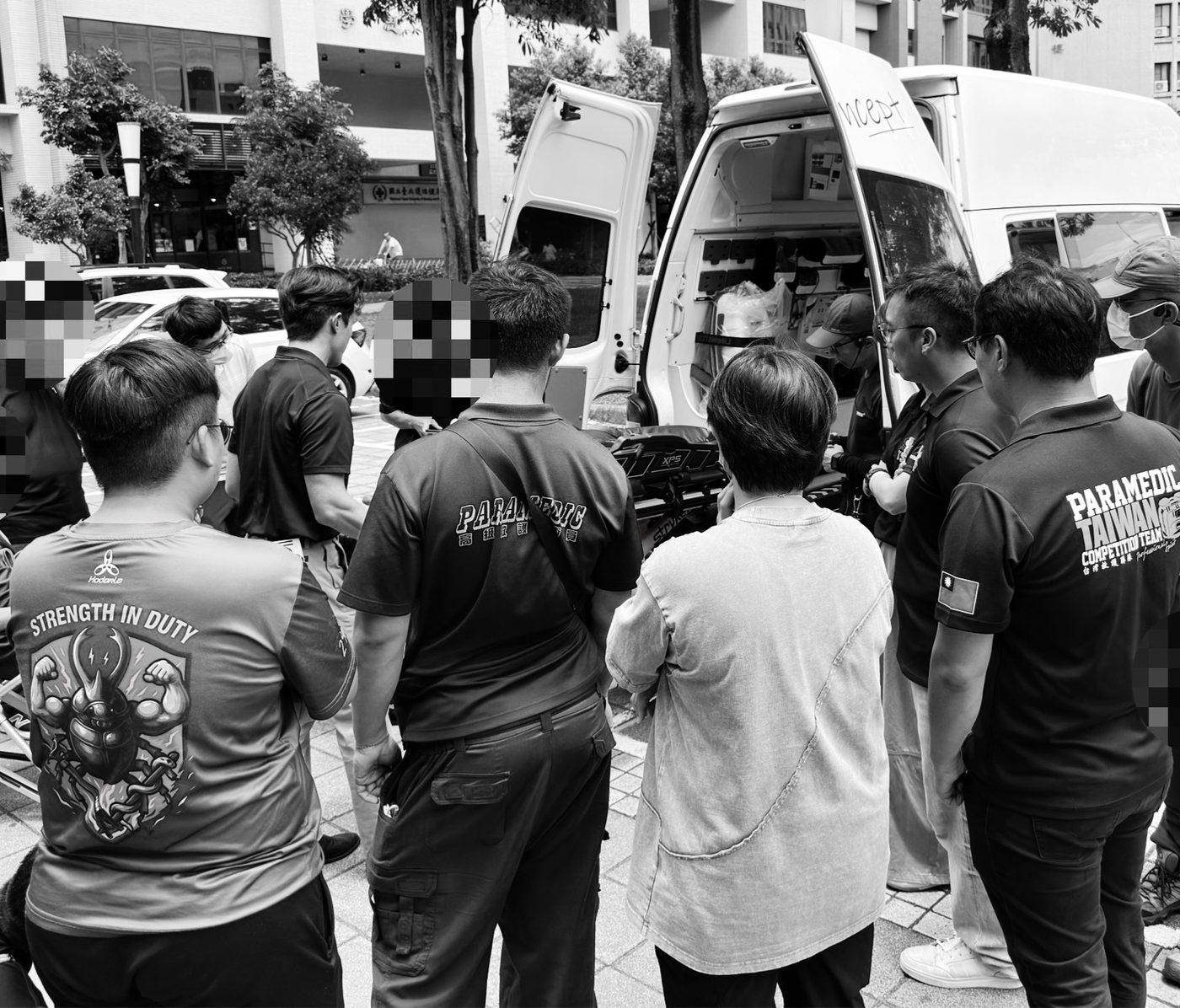 EMS 搬運安全訓練現場，救護人員圍繞救護車後艙與搬運設備討論流程